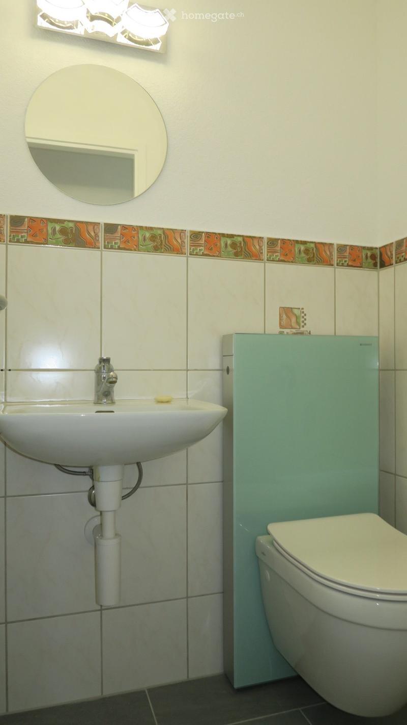 Bathroom with a white sink, chrome faucet, toilet, and a round mirror above the sink. The walls are tiled with a decorative border.