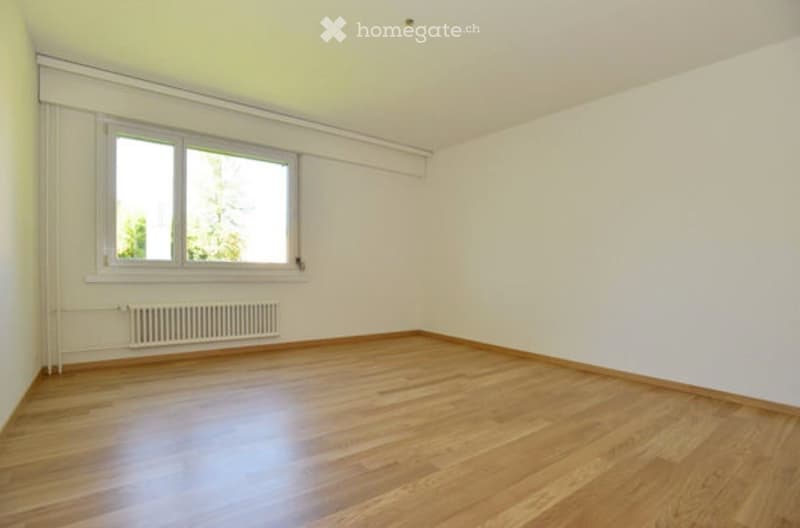 Empty room with wooden flooring, white walls, large window, and radiator.