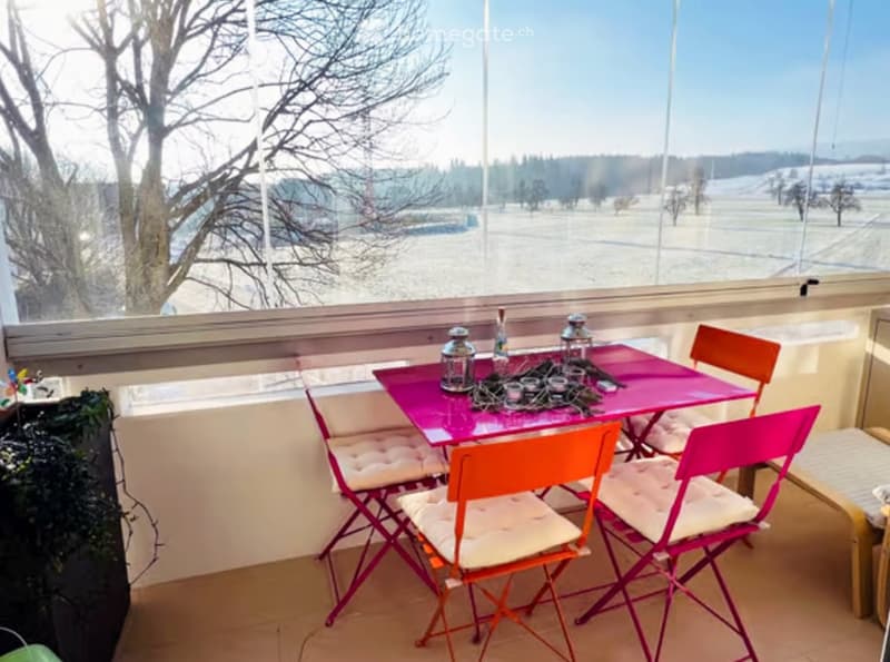 Balcony with a pink table and orange chairs, overlooking a snowy landscape.