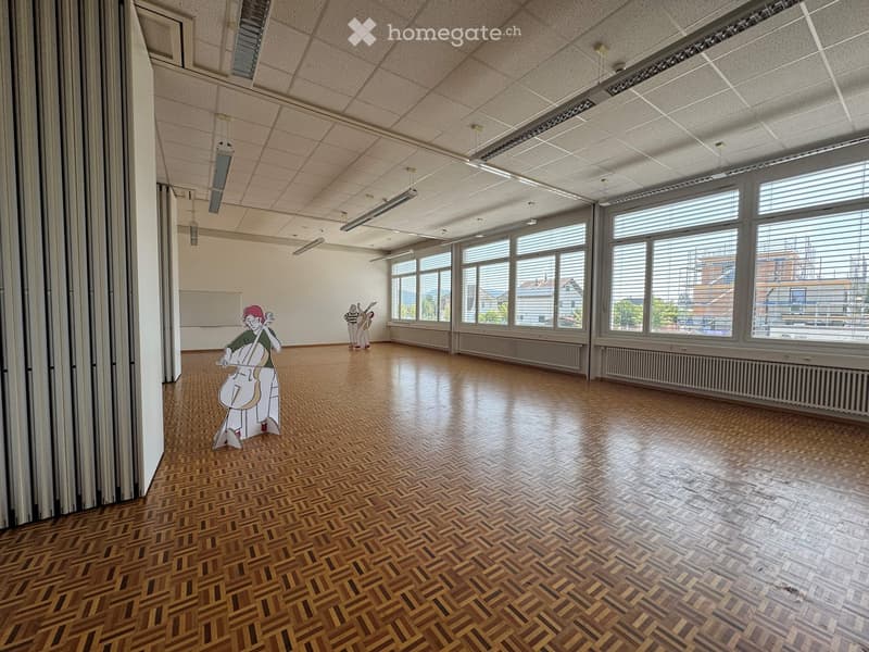 Empty room with wooden herringbone flooring, large windows with blinds, and a whiteboard on the wall. No furniture or equipment present.