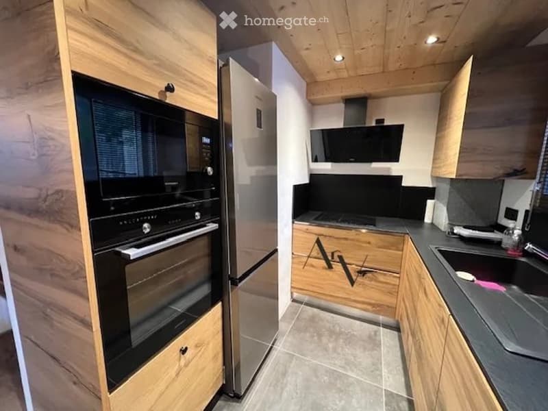 Modern kitchen with wooden cabinets, stainless steel appliances, and a sleek black oven. The space features a gray countertop, a sink, and a refrigerator, all set against a light-colored tiled floor and wooden ceiling.