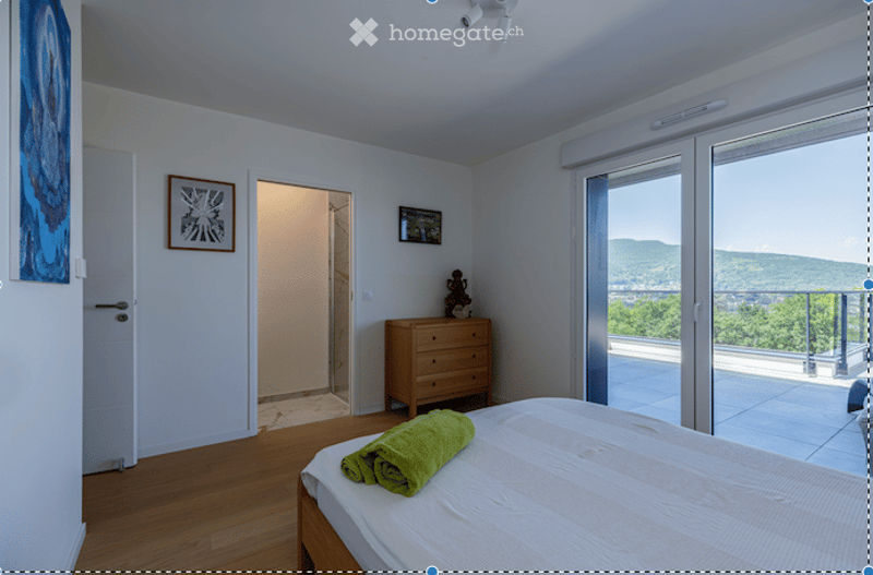 Bright bedroom with wooden flooring, large window offering a scenic view, bed with white linens, green towel, chest of drawers, and framed artwork on the wall.