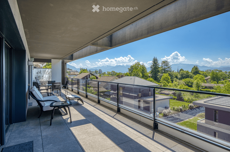 Balcony with modern furniture, glass railing, and scenic mountain view.
