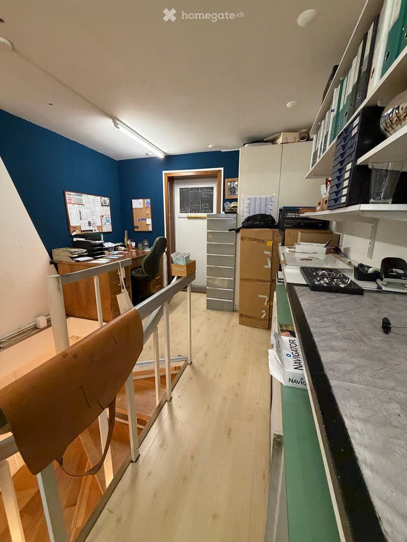 Office space with wooden flooring, blue accent wall, desk, chair, filing cabinet, shelves, and various office supplies.
