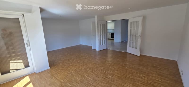 Empty room with wooden flooring, white walls, and large sliding glass doors leading to a balcony.