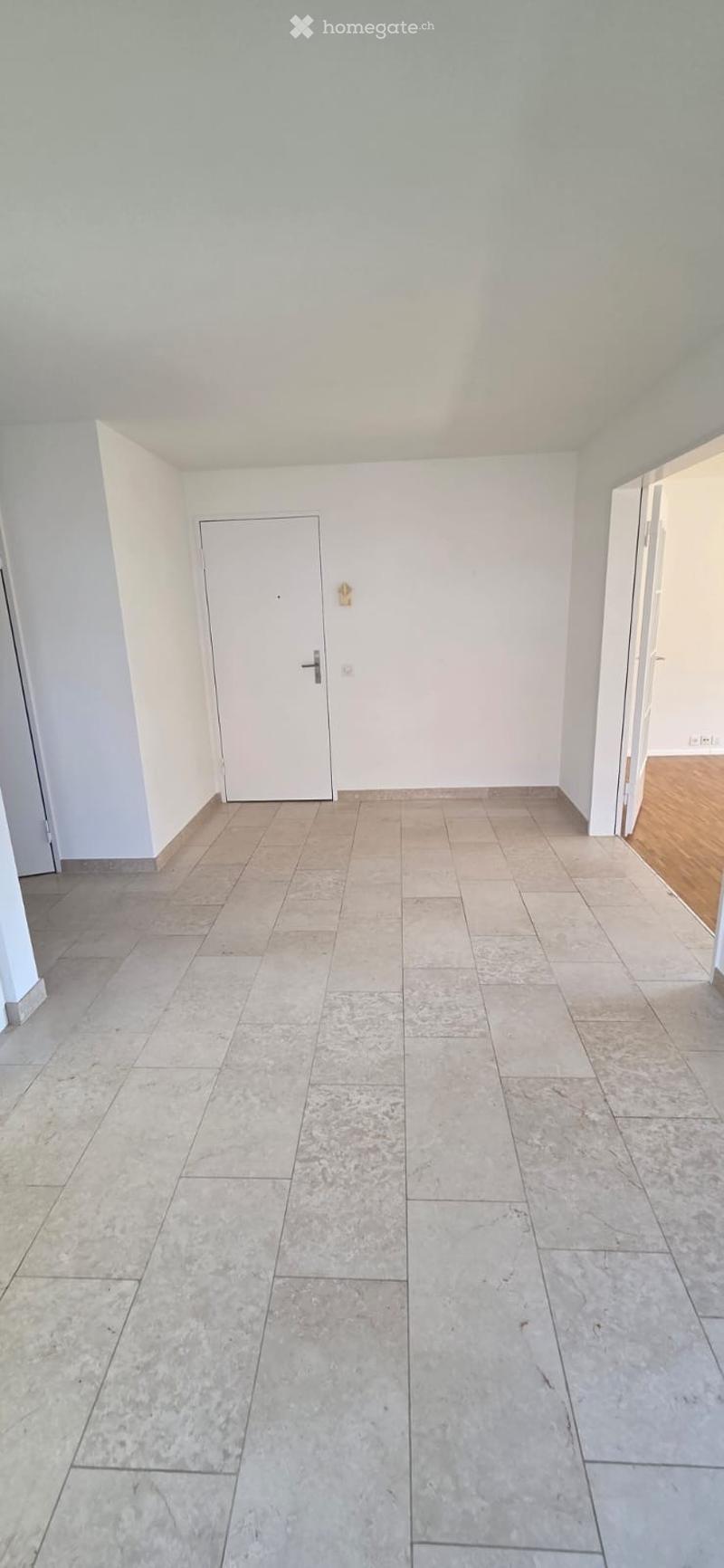 Empty room with light grey tiled floor and white walls, featuring a closed white door and a visible electrical outlet.