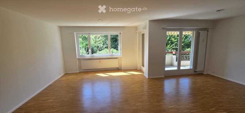 Empty room with wooden flooring, large windows, and a sliding glass door leading to a balcony.