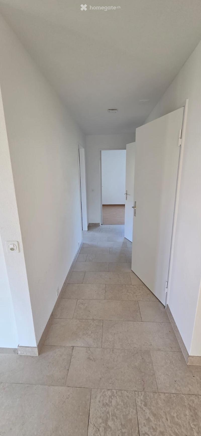 Empty hallway with tiled floor, white walls, and several doors leading to other rooms.