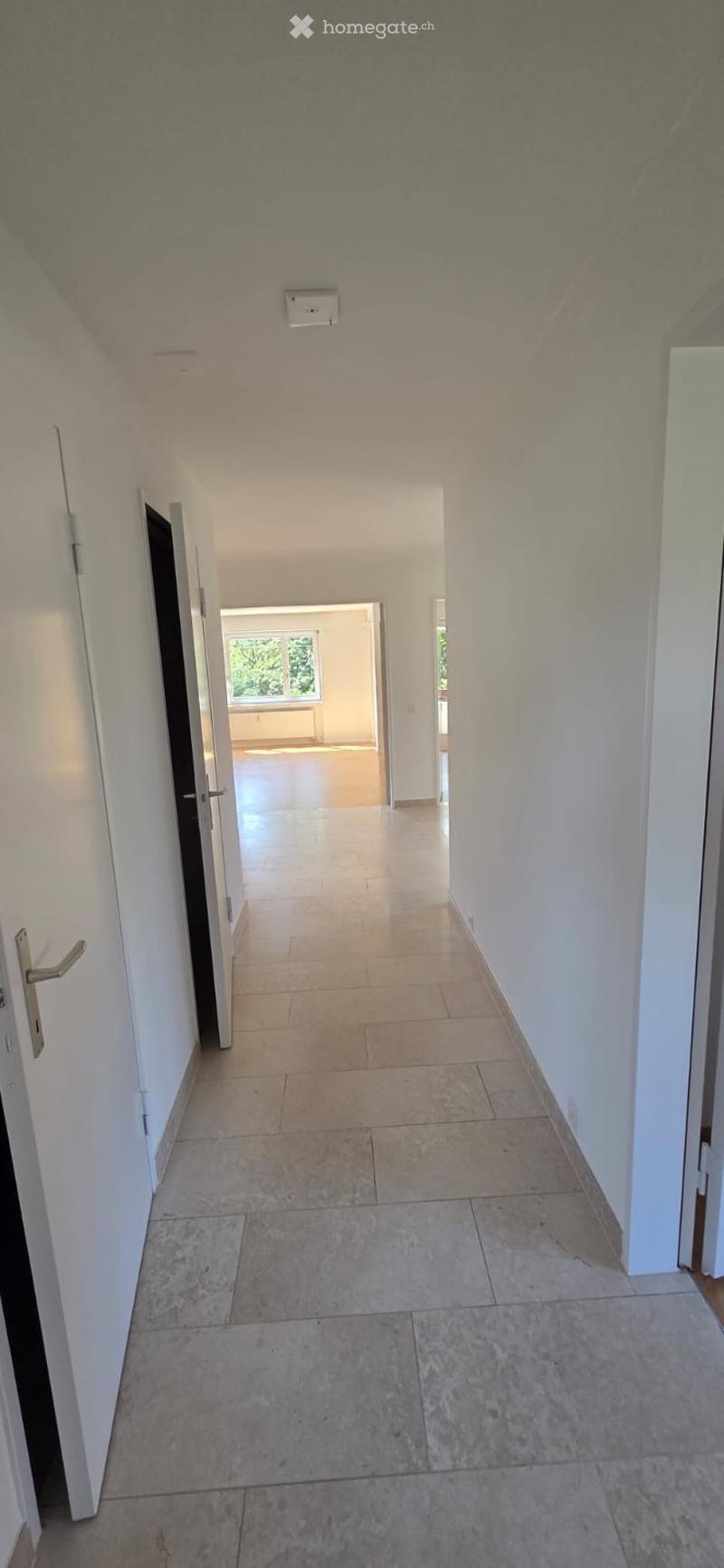 Empty hallway with tiled floor, white walls, and several doors leading to other rooms.