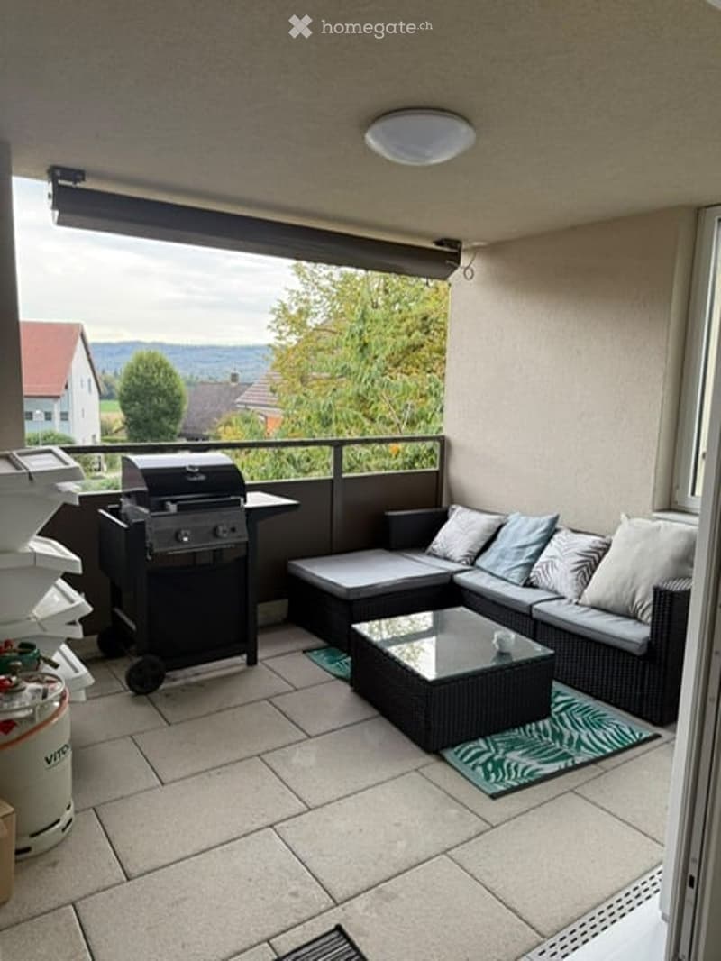 Balcony with a modern outdoor seating area, including a sofa, coffee table, and a grill, overlooking a scenic landscape.
