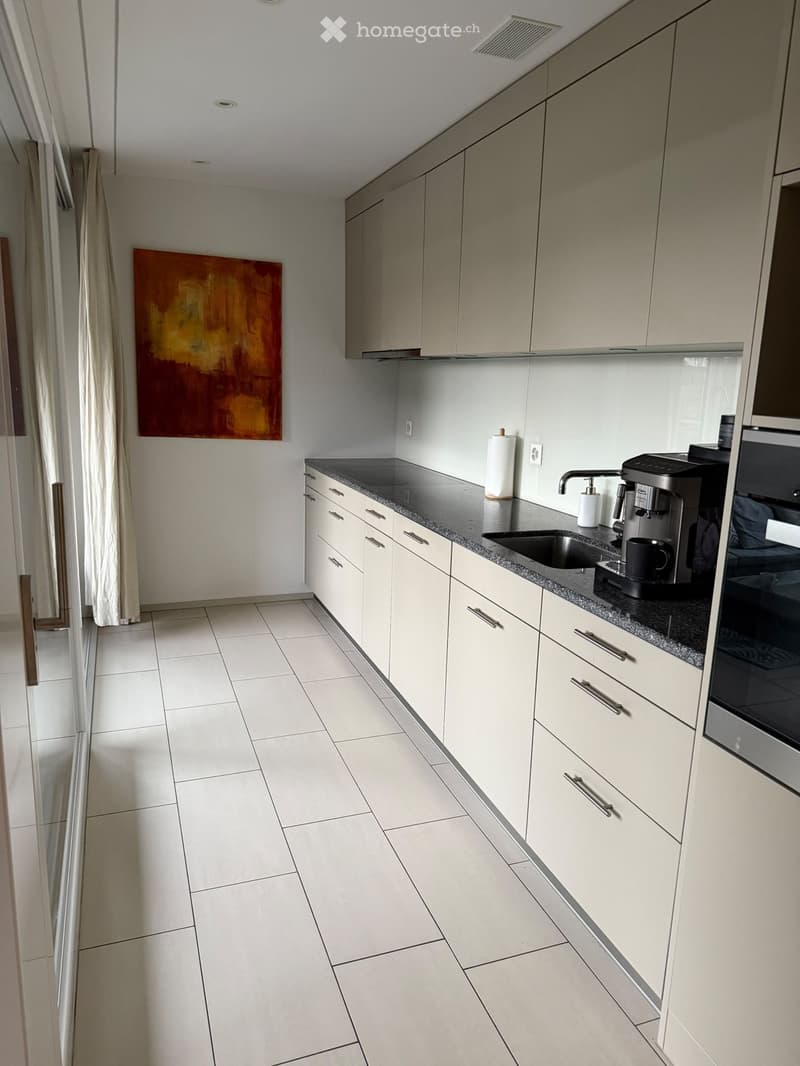 Modern kitchen with white cabinets, granite countertops, and stainless steel appliances, including a coffee maker and sink.