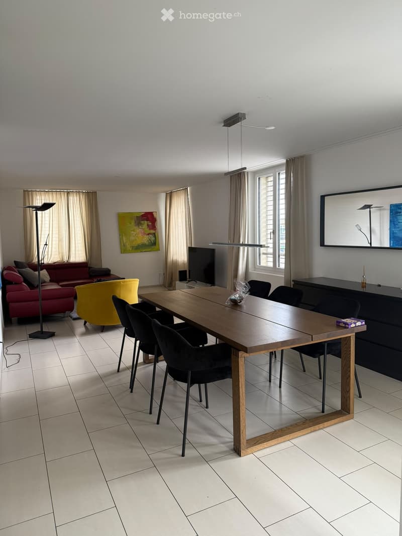 Modern living and dining area with a red sofa, yellow armchair, wooden dining table, black chairs, and a television mounted on the wall.