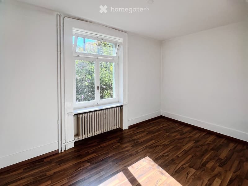 Empty room with wooden flooring, white walls, and a window with a radiator below it.