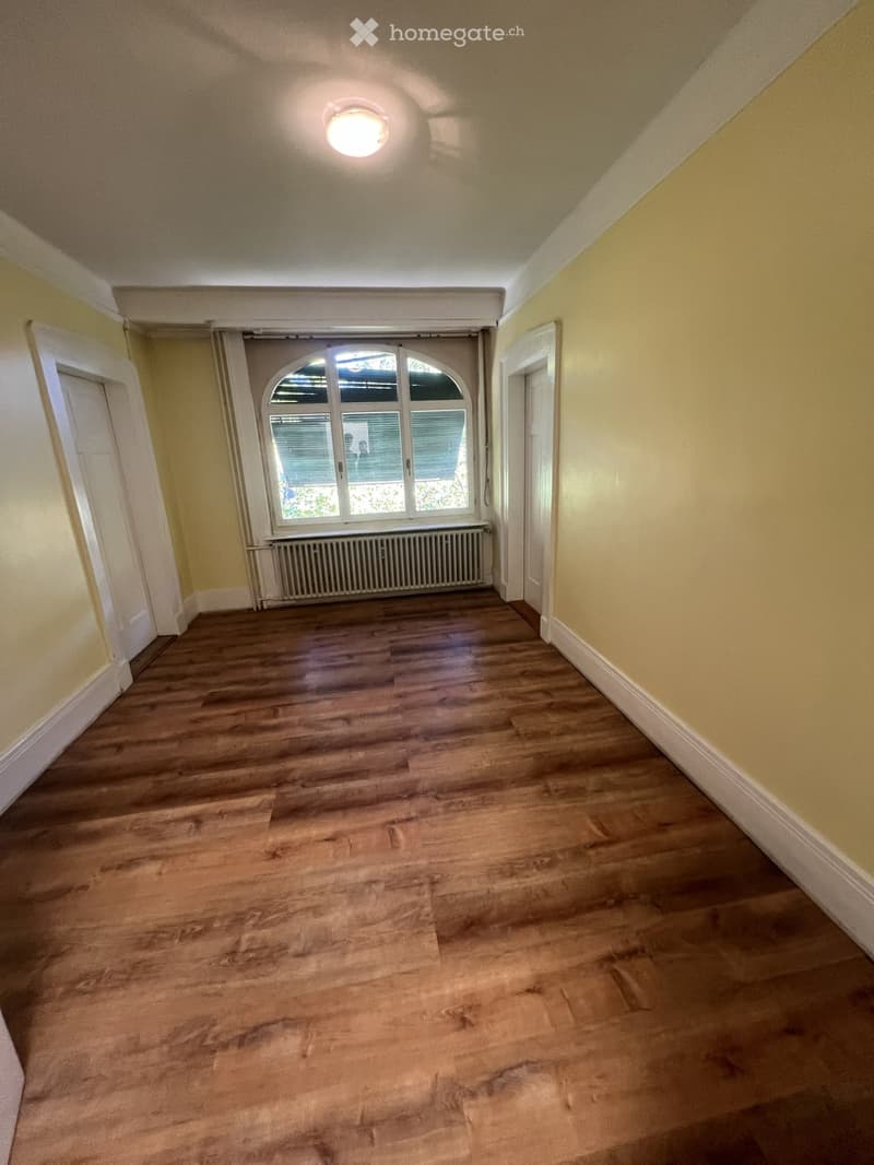 Empty hallway with wooden flooring, yellow walls, white trim, and a large arched window at the end.