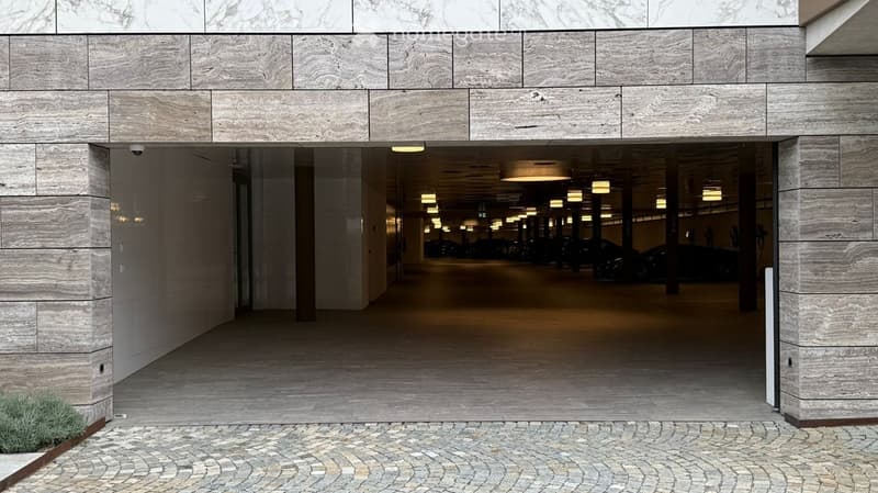 Modern building entrance with marble facade, glass doors, and a spacious underground parking area visible through the entrance.