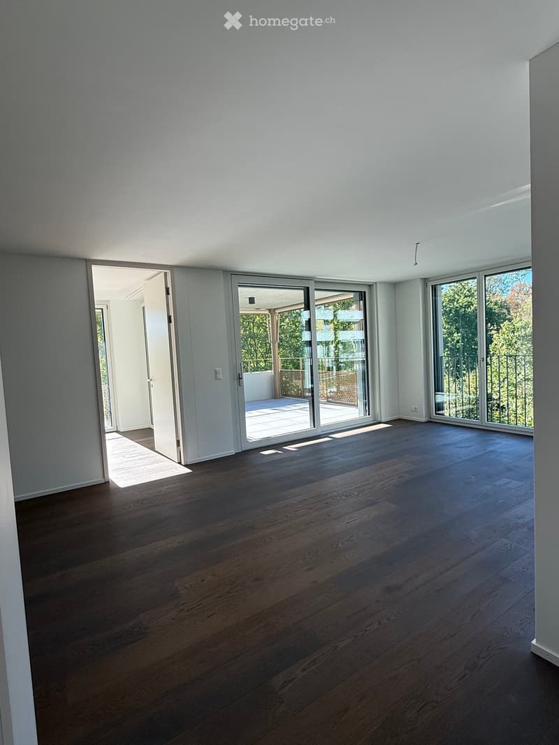 Empty room with wooden flooring, white walls, large sliding glass doors leading to a balcony, and natural light streaming in.