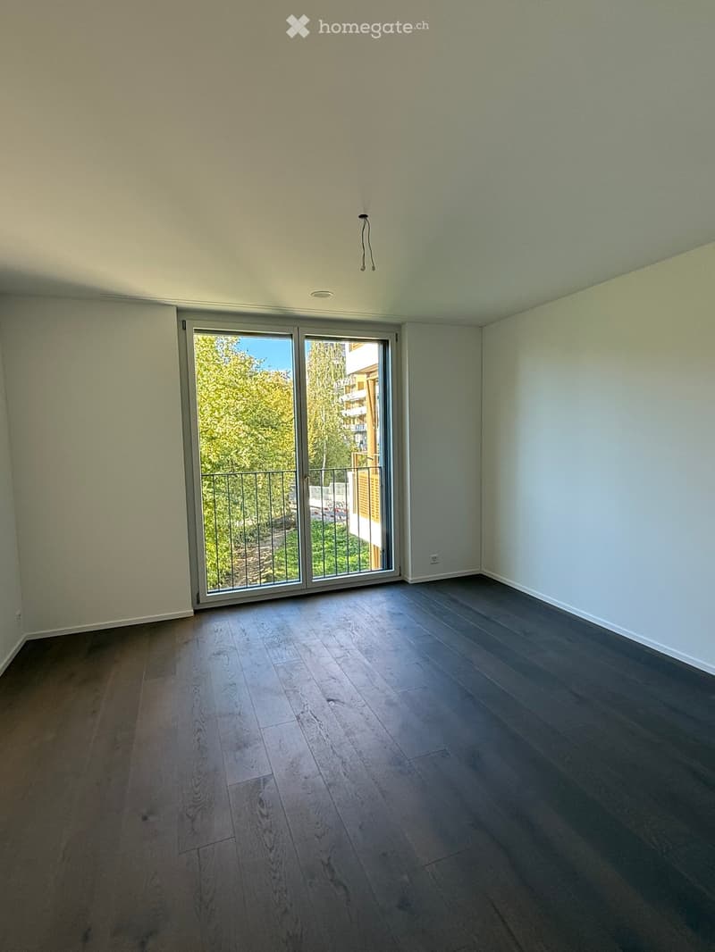 Empty room with wooden flooring, large sliding glass door leading to a balcony, and light-colored walls.