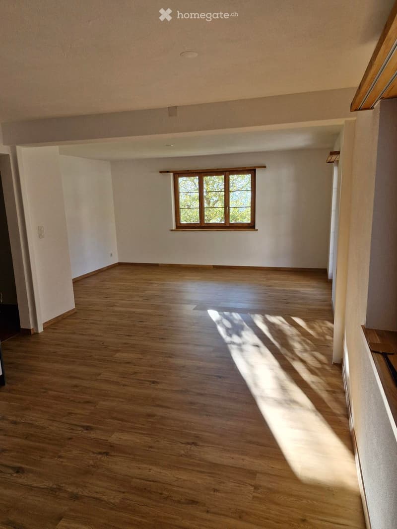 Empty room with wooden flooring and white walls, featuring a single window with wooden frame and natural light streaming in.