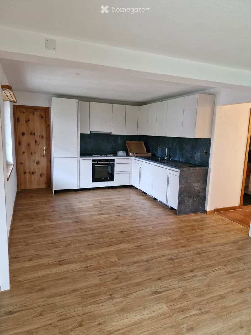 Empty kitchen with white cabinets, wooden floor, and a dark countertop. No appliances or furniture are present.
