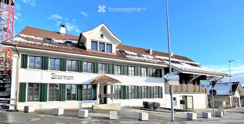 A two-story white building with green shutters and a red-tiled roof, featuring a sign that reads "Sternen" and a small entrance area.