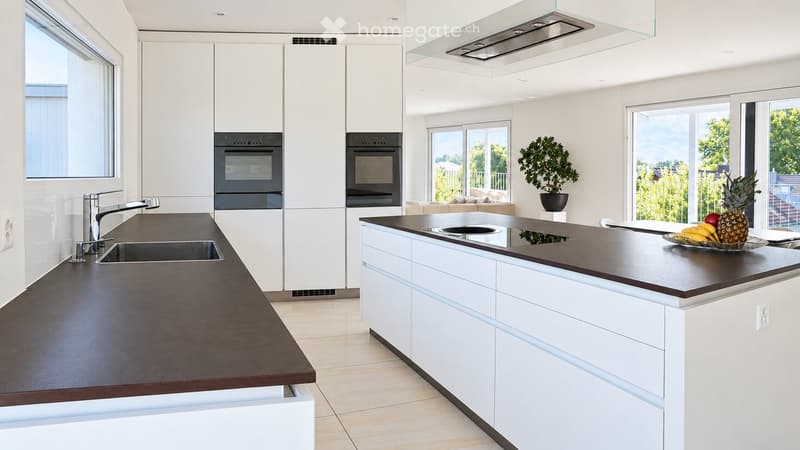 Modern kitchen with white cabinets, dark countertops, stainless steel appliances, and a bowl of fruit on the island.