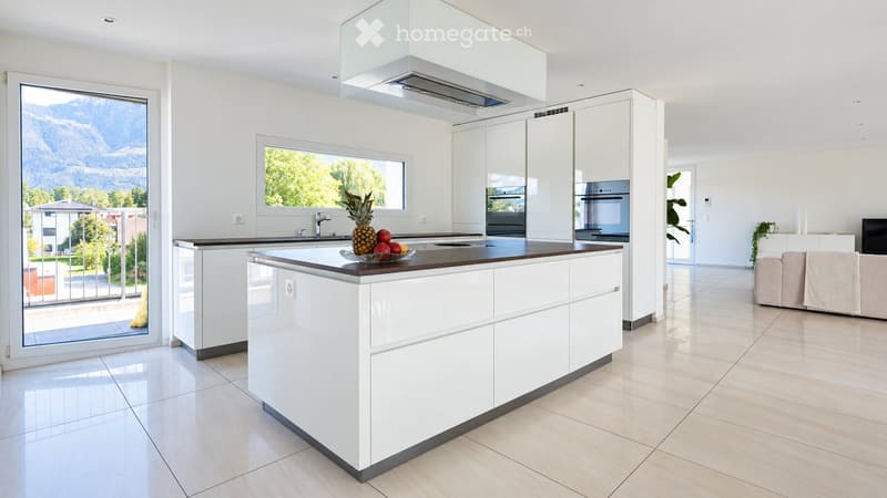 Modern kitchen with white cabinets, island, stainless steel appliances, and a view of mountains through large windows.