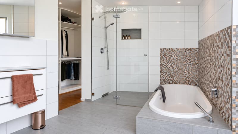 Modern bathroom with a bathtub, glass-enclosed shower, built-in closet, and a towel on the counter.