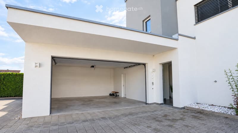 Modern two-story house with a large garage, white exterior, and a small balcony on the upper level.