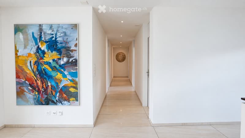 Modern hallway with white walls, light wooden flooring, and contemporary artwork displayed on the walls.