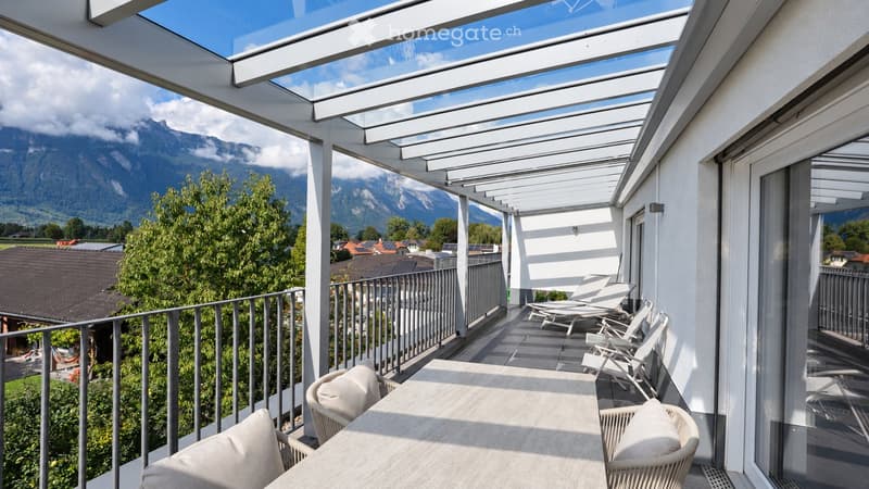 Balcony with a retractable roof, offering a scenic mountain view, furnished with a table and chairs.