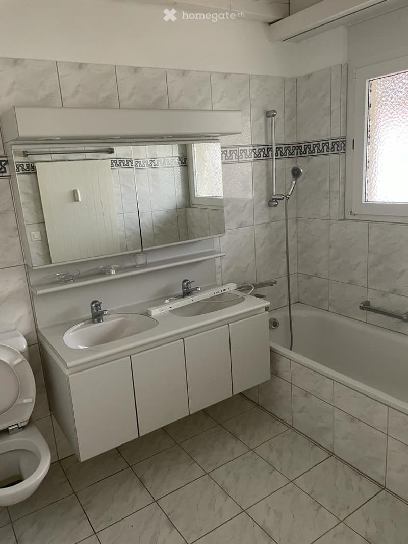 Modern bathroom with marble tiles, double sink vanity, large mirror, bathtub, and shower fixture.