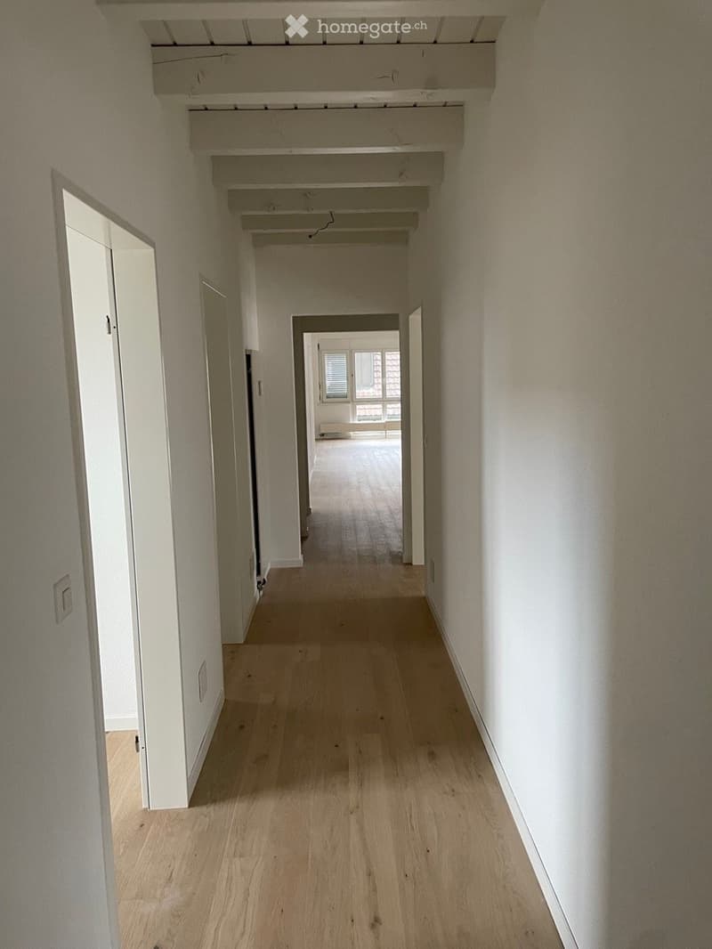 Empty hallway with light wooden flooring, white walls, and several open doors leading to other rooms.