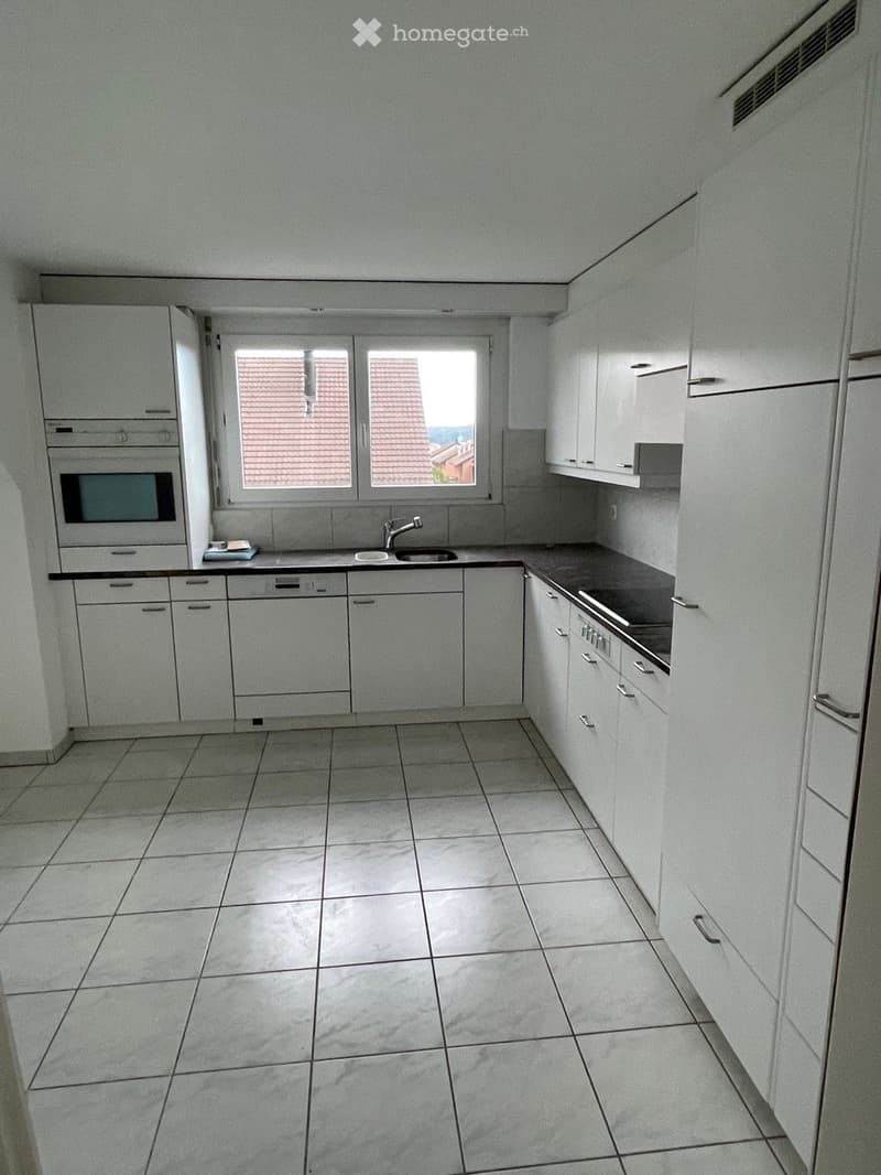 Empty kitchen with white cabinets, tiled floor, and a window overlooking a tiled roof.