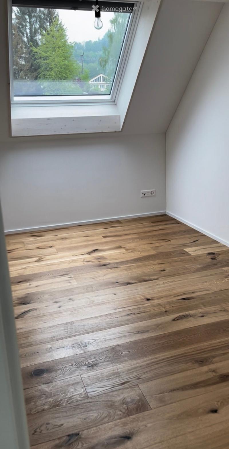 Empty room with wooden flooring and white walls, featuring a skylight window and a visible electrical outlet.
