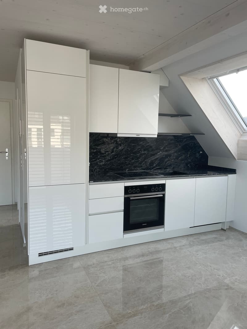 Modern kitchen with white cabinets, a stainless steel refrigerator, an oven, and an induction cooktop, featuring a dark marble backsplash and light marble flooring.