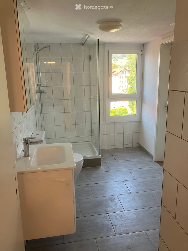Modern bathroom with a white sink, chrome faucet, toilet, glass-enclosed shower, and a large window offering a view of the outside.
