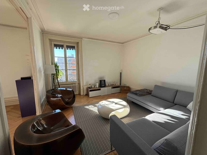 Modern living room with a grey sectional sofa, white coffee table, two brown leather chairs, a small table with a lamp, and a projector screen on the ceiling.