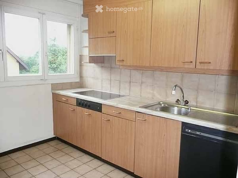 Modern kitchen with light wooden cabinets, tiled countertops, and stainless steel sink and dishwasher.