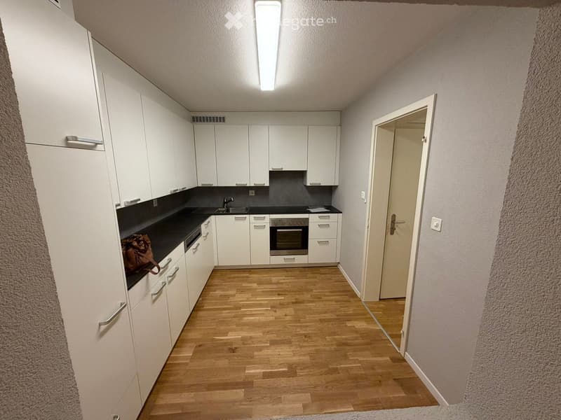 Modern kitchen with white cabinets, black countertops, wooden flooring, and a small handbag placed on the counter.