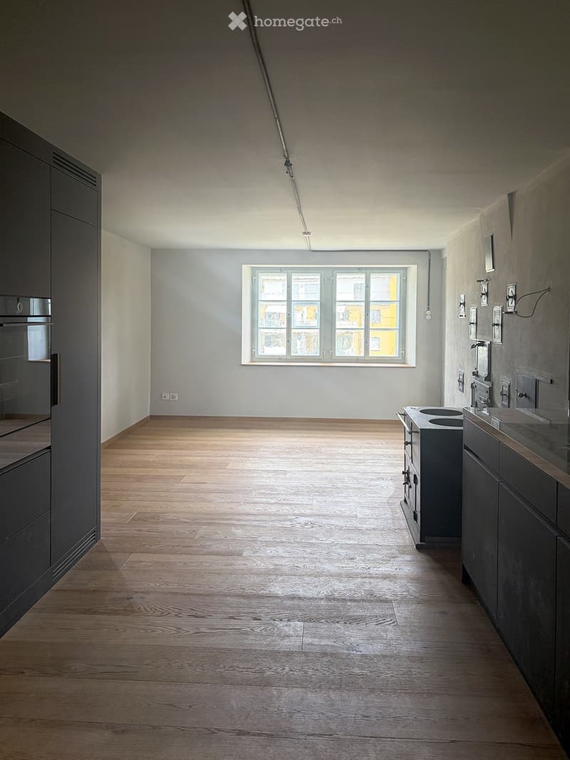 Empty room with wooden flooring, white walls, and a large window letting in natural light. Minimalist design with no furniture or appliances.