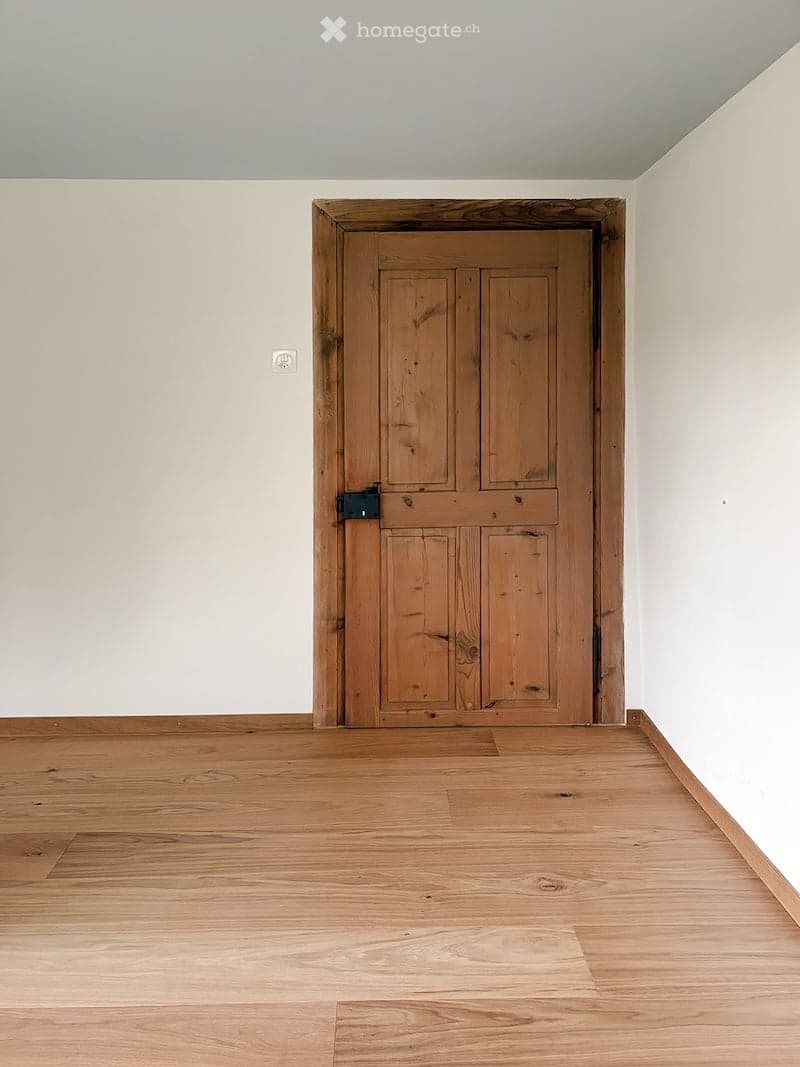Empty room with wooden floor and a single wooden door. No furniture or equipment present.