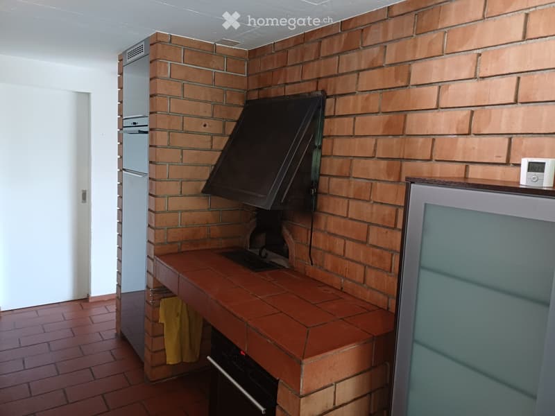 Brick-walled kitchen with a wooden countertop, built-in oven, and refrigerator. A yellow jacket is hanging on the wall.