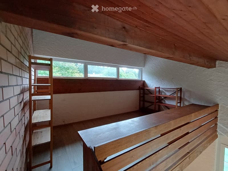 Empty room with wooden ceiling, brick wall, and wooden shelves. No furniture or equipment present.