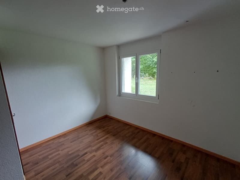 Empty room with wooden flooring and white walls, featuring a single window with white frame and a door on the left side.