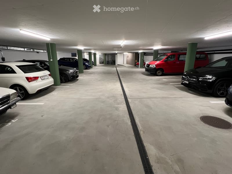 Underground parking area with several parked cars, green support pillars, and a concrete floor.