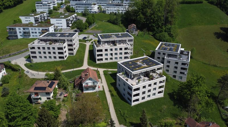 Aerial view of a residential area with multiple modern apartment buildings, green lawns, pathways, and solar panels on rooftops.
