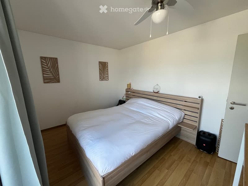 Cozy bedroom with a wooden bed, white bedding, nightstand, wall art, and a ceiling fan.