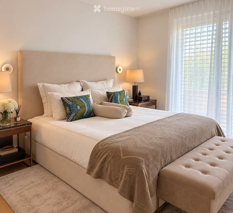 Elegant bedroom with a large bed, decorative pillows, a nightstand with a lamp, a bench at the foot of the bed, and a vase with flowers on a side table.