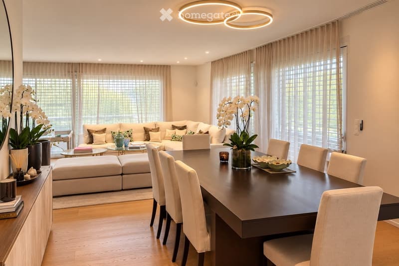 Modern living and dining area with a white sectional sofa, coffee table, ottoman, dining table with chairs, decorative vases, and a large mirror. The space features large windows with sheer curtains and recessed lighting.