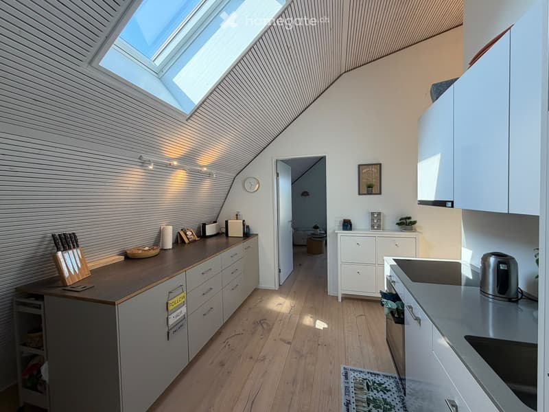 Modern kitchen with white cabinets, wooden countertops, and a skylight above. Includes a knife block, toaster, bowl, and small plant on the counter.